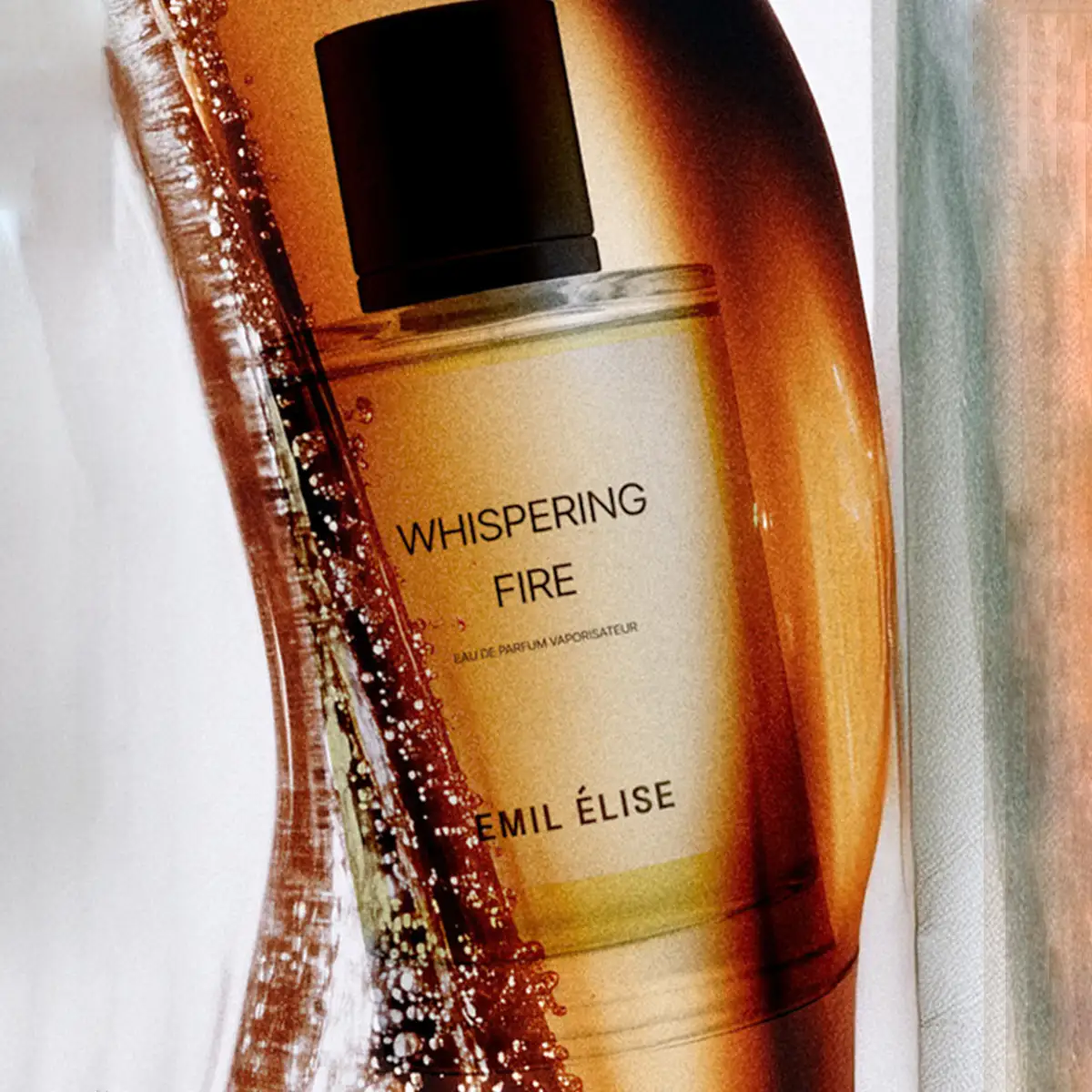 Emil Élise - whispering fire Parfümflakon mit klarem Glas und schwarzem Verschluss in warmem Lichtspiel vor hellem Hintergrund
