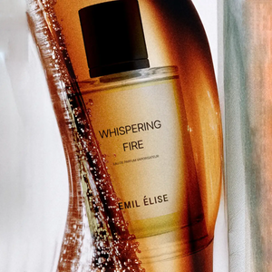 Emil Élise - whispering fire Parfümflakon mit klarem Glas und schwarzem Verschluss in warmem Lichtspiel vor hellem Hintergrund