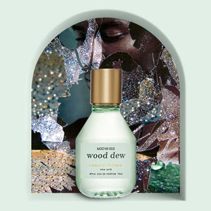Nomenclature - wood dew Parfumflakon mit milchigem Glas und goldfarbenem Verschluss vor künstlerischem Hintergrund