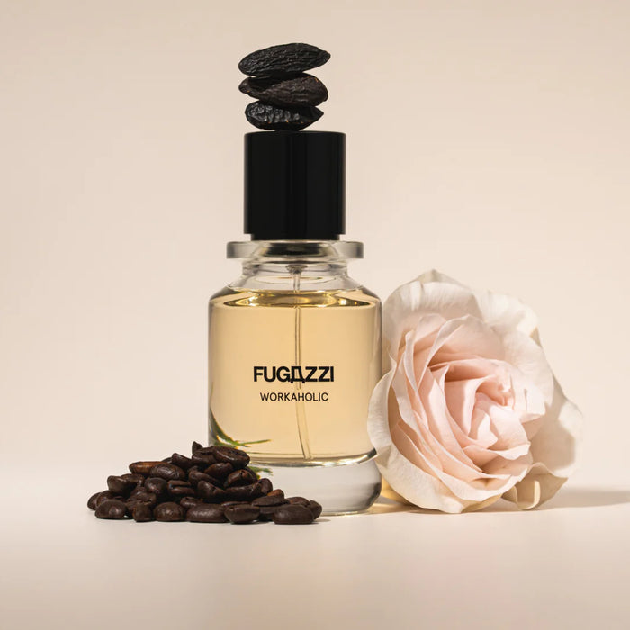 Fugazzi - Workaholic Parfumflakon mit hellgelbem Duft, schwarzem Deckel, Kaffeebohnen und zarter rosa Blume vor beigem Hintergrund