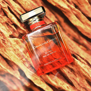 Ormonde Jayne - Xi'an Parfumflakon in warmem Orangeton mit transparentem Verschluss auf strukturierter Holzoberfläche