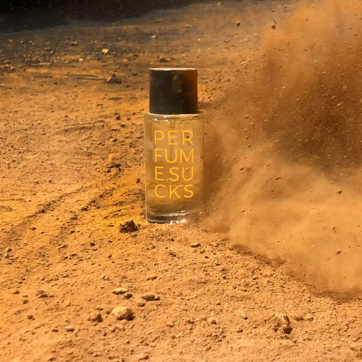 PERFUME.SUCKS - Yellow 130C Flakon mit schwarzem Deckel und gelber Schrift in staubiger Wüstenlandschaft