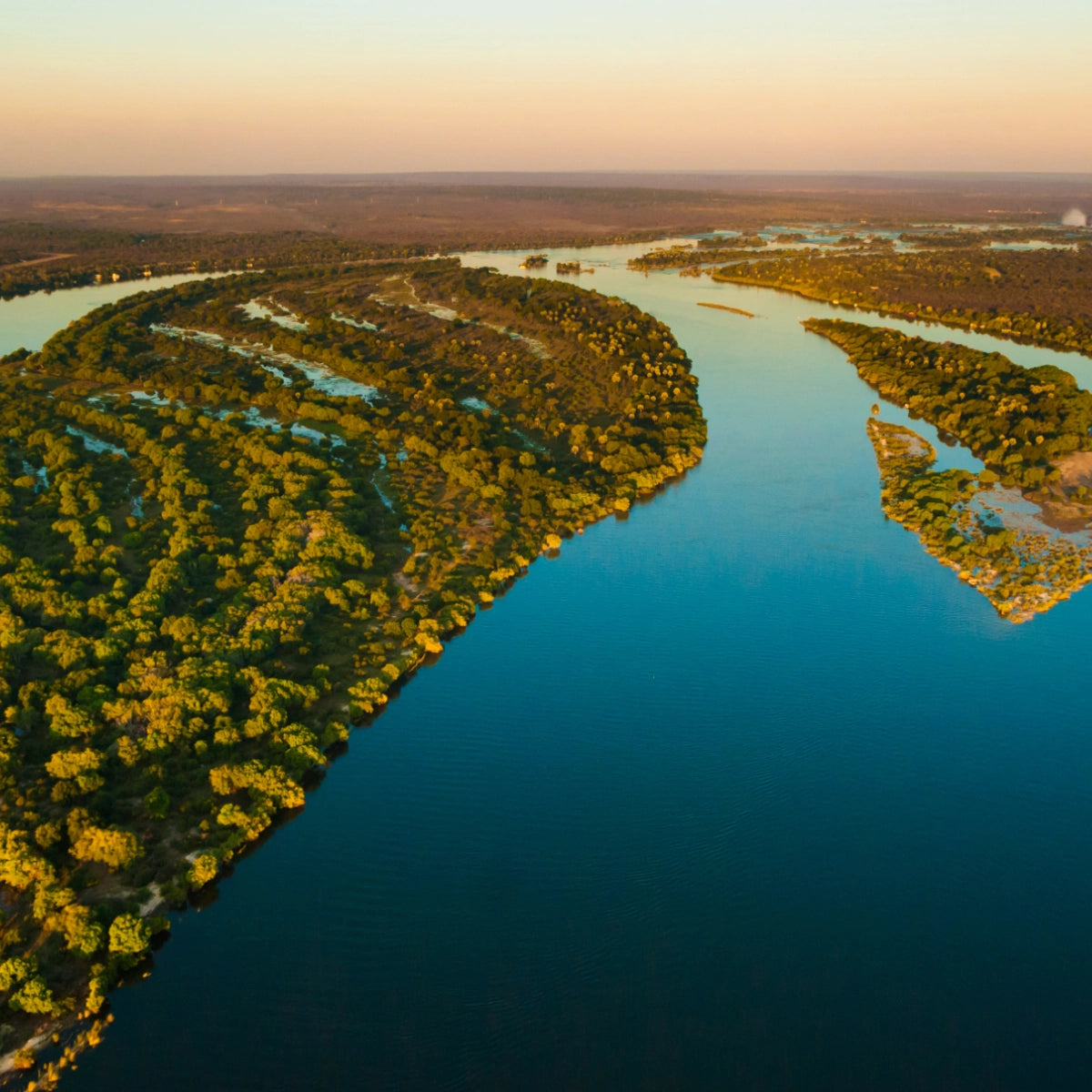 Olfattology - Zambesi Luftaufnahme des Sambesi-Flusses mit üppiger Vegetation und weiter Flusslandschaft bei Sonnenuntergang