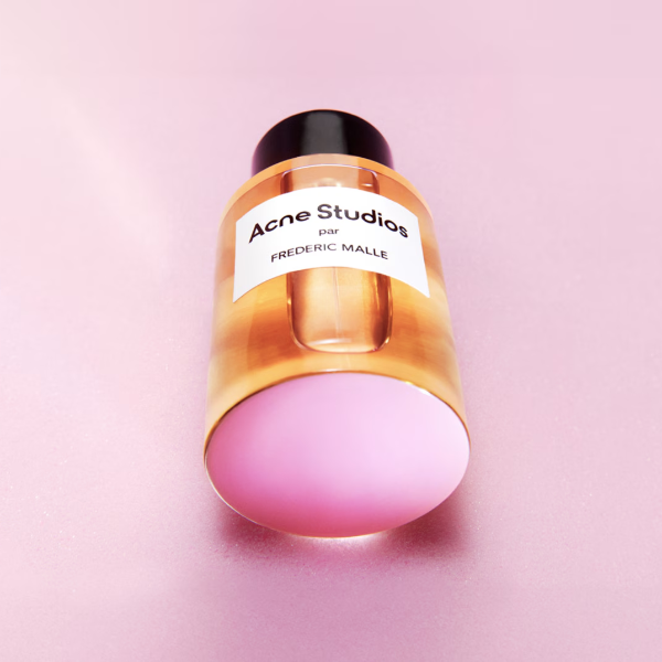Frédéric Malle - Acne Studios by Frédéric Malle Parfümflakon mit schwarzem Deckel auf rosa Hintergrund liegend