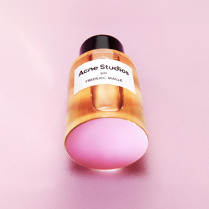 Frédéric Malle - Acne Studios by Frédéric Malle Parfümflakon mit schwarzem Deckel auf rosa Hintergrund liegend