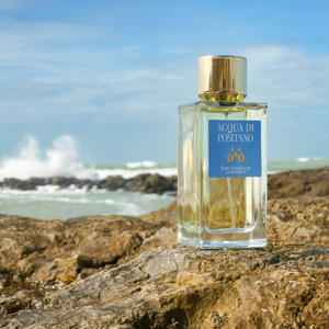 Eau d'Italie - Acqua di Positano Parfümflakon mit goldenem Verschluss und hellem blauem Etikett am felsigen Meeresufer