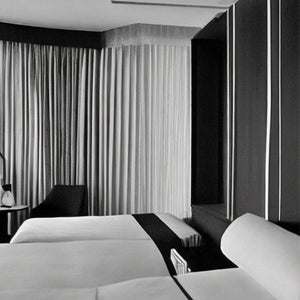 Pantomime - Act 1: Elegantes Hotelzimmer mit zwei Betten, Vorhängen und minimalistisch gestaltetem Interieur in Schwarzweiß