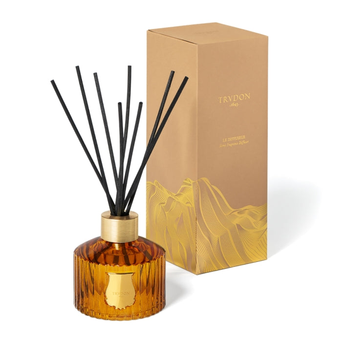 Trudon - Altaïr - Diffusor bernsteinfarbene Glasflasche mit goldfarbenem Verschluss und schwarzen Stäbchen vor heller Verpackung