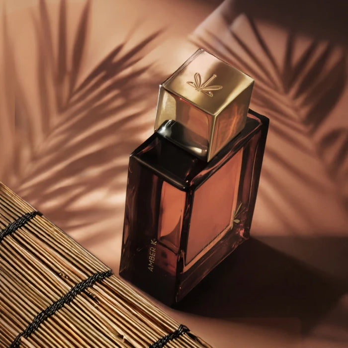 Ella K - Amber K Parfumflakon mit bernsteinfarbenem Glas und goldfarbenem Deckel vor warmem Schattenmuster