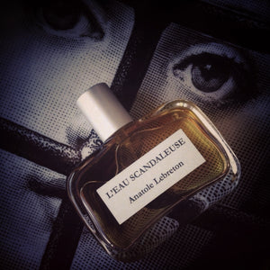 Anatole Lebreton - L’Eau Scandaleuse Parfumflakon mit bernsteinfarbener Flüssigkeit vor grafischem Augenmotiv