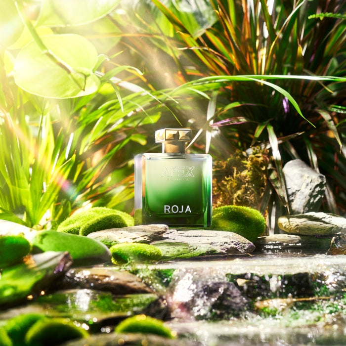 Roja Parfums - APEX Eau Intense zeigt grünen Flakon eingebettet in natürliche Landschaft mit Wasser und Pflanzenlichtspiel
