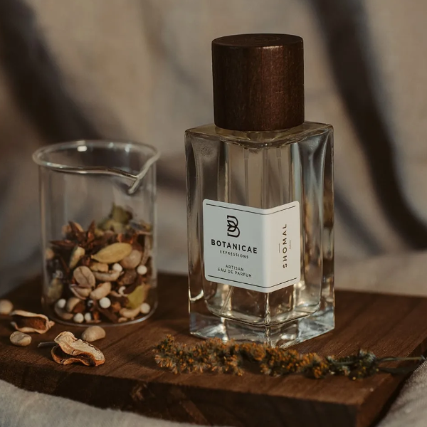 Botanicae - Shomal Parfumflakon mit dunkelbraunem Holzverschluss auf Holzbrett neben Gewürzen vor sanftem Hintergrund
