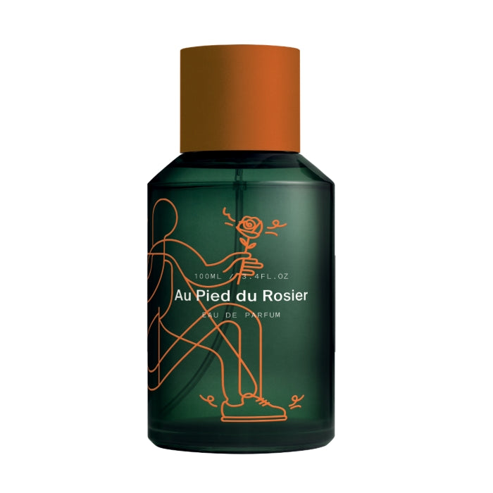Marie Jeanne - Au Pied du Rosier zeigt grünen Flakon mit grafischer orangener Linie und mattem orangenem Verschluss auf weißem Grund