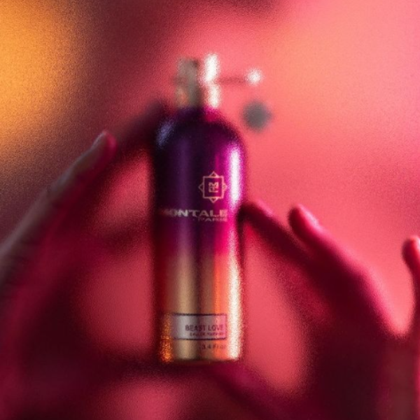 Montale - Beast Love Flakon mit pink-goldenem Verlauf in schimmernder, warmer Atmosphäre gehalten von Händen