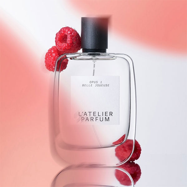 L'Atelier Parfum - Opus 1 - Belle Joueuse klarer Flakon mit schwarzem Verschluss und frischen Himbeeren auf rosafarbenem Hintergrund