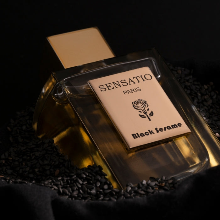 Sensatio Paris - Black Sesame Flakon mit goldfarbenem Verschluss liegt auf schwarzem Sesam in dunklem Ambiente