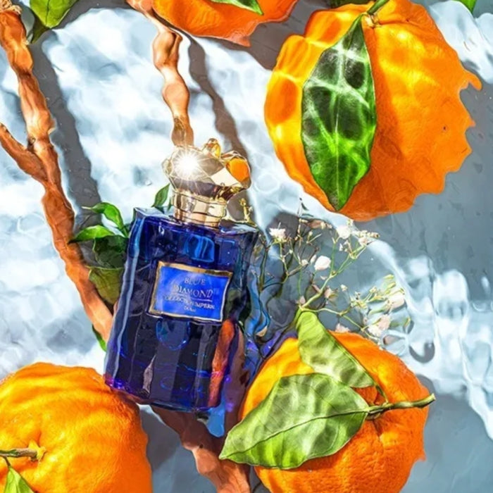 Imperial Parfums - Blue Diamond blauer Flakon mit goldenem Verschluss umgeben von leuchtenden Mandarinen und Blättern