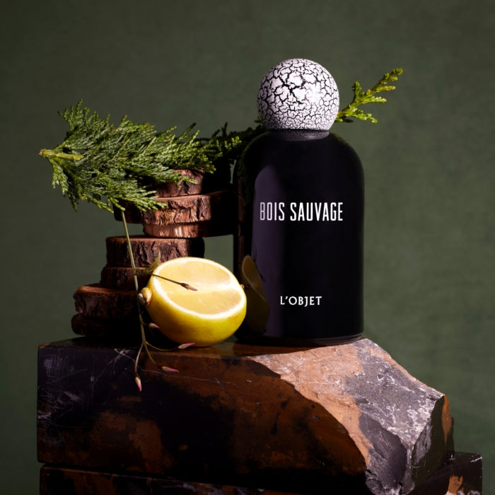 L'Objet - Bois Sauvage Parfumflakon in tiefschwarzem Glas mit markantem, weiß-rissigem Kugelverschluss und natürlicher Inszenierung