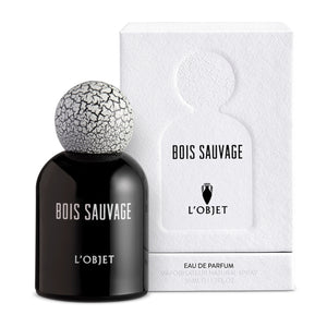 L'Objet - Bois Sauvage Parfumflakon in schwarzem Glas mit weiß-rissigem Kugelverschluss vor weißer Verpackung
