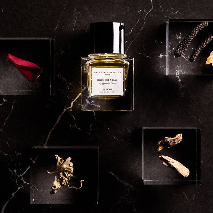 Essential Parfums - Bois Impérial - Extrait de Parfum klarer Flakon auf dunklem Marmor mit natürlichen Duftnoten arrangiert