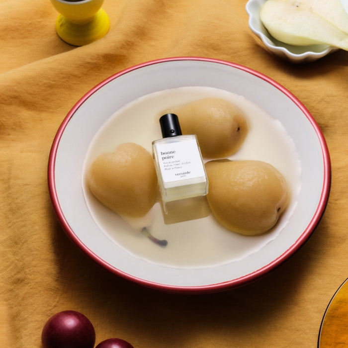 Versatile - Bonne Poire Flakon mit schlichtem Design auf Teller mit drei Birnen in milchiger Flüssigkeit