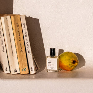 Versatile - Bonne Poire Parfumflakon mit schwarzem Verschluss neben reifer Birne und Büchern im Sonnenlicht
