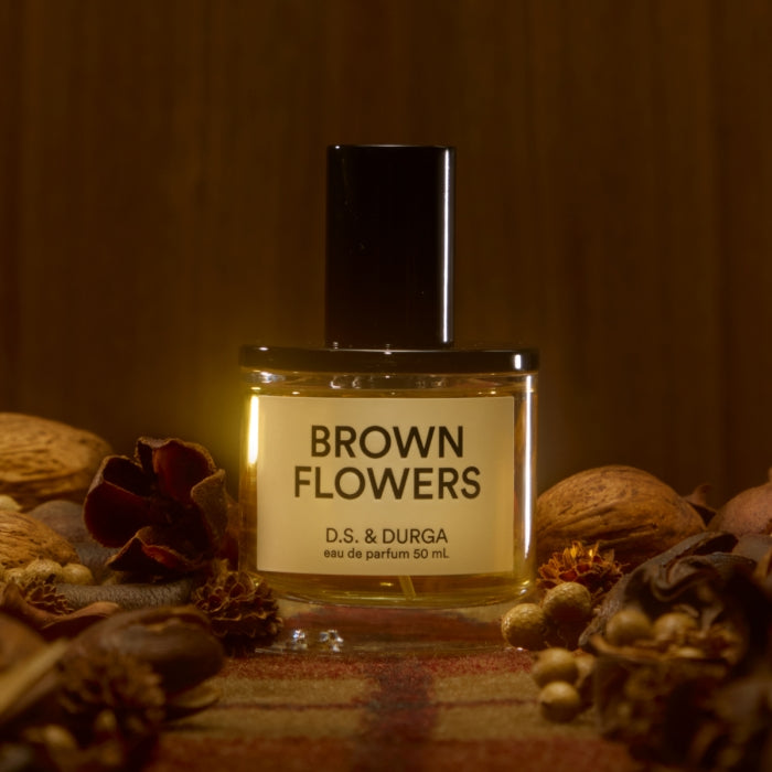 D.S. & Durga - Brown Flowers zeigt Flakon mit brauner Flüssigkeit umgeben von getrockneten Blüten und Gewürzen