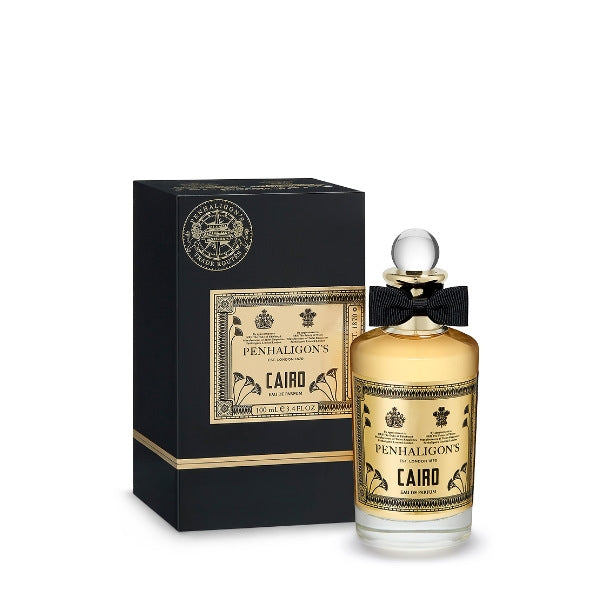 Penhaligon's - Trade Routes - Cairo Parfumflakon mit goldfarbenem Etikett und schwarzer Schleife neben schwarzer Geschenkbox