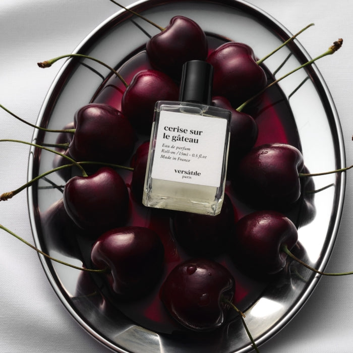 Versatile - Cerise sur le Gâteau Parfumflakon auf Silbertablett umgeben von dunklen Kirschen und Lichtreflexen
