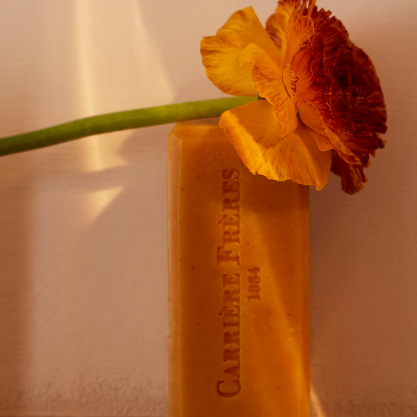 Carrière Frères - Silvae - Seife als bernsteinfarbener Block mit geprägtem Logo und orangefarbener Blüte im warmen Licht