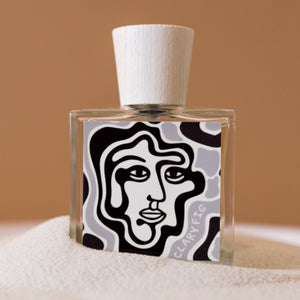 Carl Kling Parfums - Clary Fig mit modernem Flakon und stilisiertem Gesichtsmotiv vor warmem sandfarbenem Hintergrund