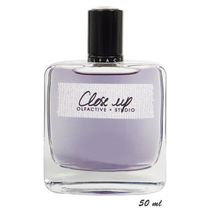 Olfactive Studio - Close Up Parfumflakon mit schwarzem Verschluss und leicht violettem Duft im klaren Glas vor weißem Hintergrund
