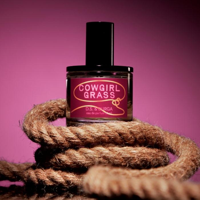 D.S. & Durga - Cowgirl Grass Parfumflakon mit rundem Design und markantem pinkfarbenem Etikett vor violettem Hintergrund
