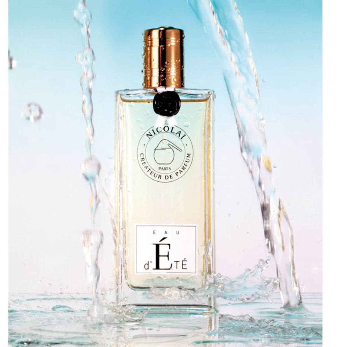 Nicolaï Eau d'Été perfume in clear rectangular bottle with gold cap surrounded by splashing water on pastel background
