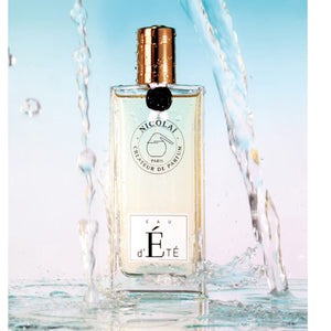 Nicolaï Eau d'Été perfume in clear rectangular bottle with gold cap surrounded by splashing water on pastel background