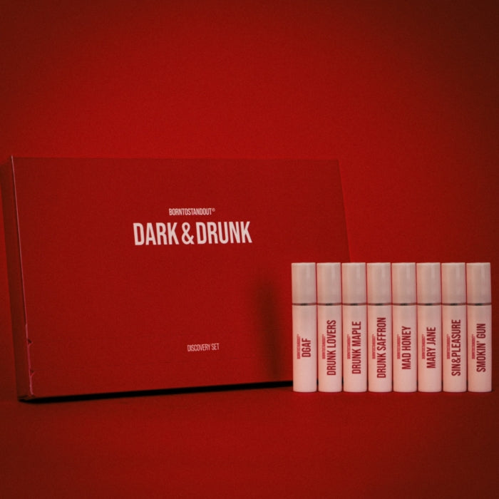 BORNTOSTANDOUT - Dark & Drunk Discovery Set mit acht Duftproben vor rotem Hintergrund elegant arrangiert