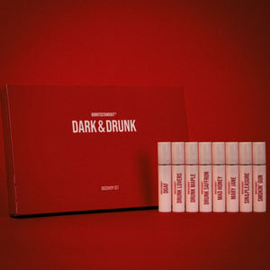 BORNTOSTANDOUT - Dark & Drunk Discovery Set mit acht Duftproben vor rotem Hintergrund elegant arrangiert