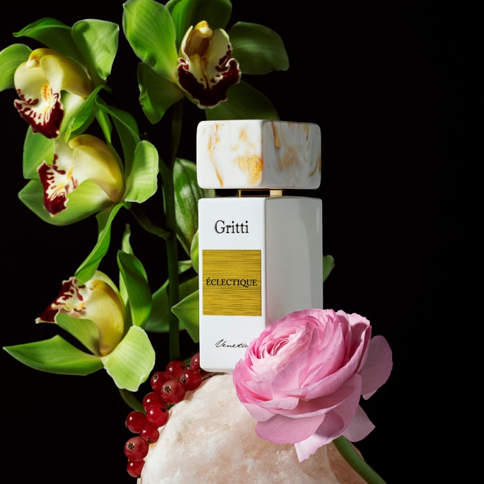 Gritti - White Collection - Eclectique zeigt weißen Flakon mit goldfarbenem Etikett zwischen Orchideen und rosa Blüte vor schwarzem Hintergrund