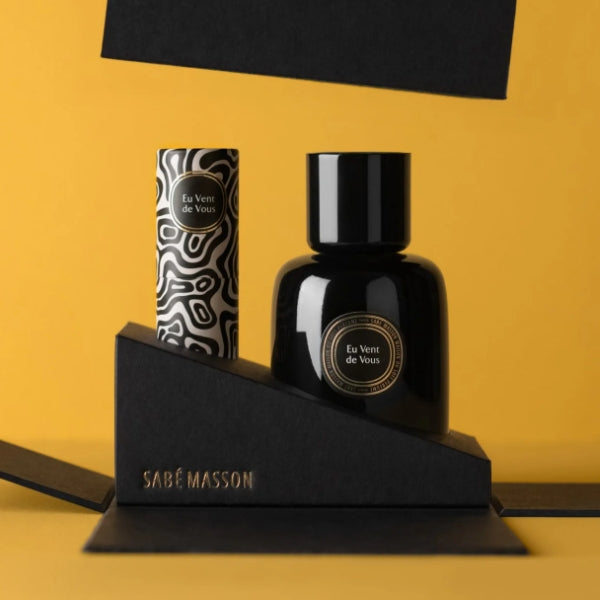 Sabé Masson - Eu Vent de Vous - La Rencontre schwarzes Parfumfläschchen und edler Lippenstift mit dekorativer Verpackung vor gelbem Hintergrund