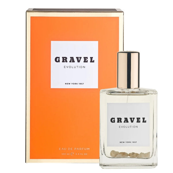 Gravel - Evolution zeigt klaren Flakon mit goldfarbenem Verschluss und beigem Quarzboden vor orangenem Hintergrund