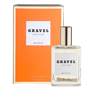 Gravel - Evolution zeigt klaren Flakon mit goldfarbenem Verschluss und beigem Quarzboden vor orangenem Hintergrund