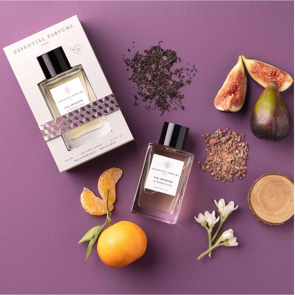 Essential Parfums - Fig Infusion Parfumflakon mit schwarzem Verschluss, frischen Feigen und Zitrusfrüchten auf violettem Hintergrund