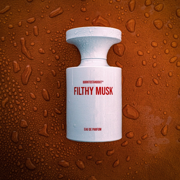 BORNTOSTANDOUT - Filthy Musk Parfumflakon in weiß mit roter Schrift vor tropfenbedecktem braunem Untergrund