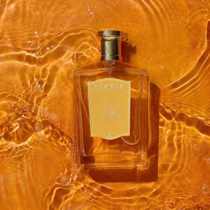 Floris - Golden Amber Parfumflakon mit goldenem Verschluss auf orangefarbenem, lichtreflektierendem Hintergrund