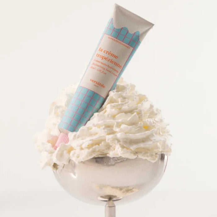 Versatile - La Crème Tropézzienne - Handcream in pastellblauer Tube steckend in Sahnehaube auf silbernem Ständer