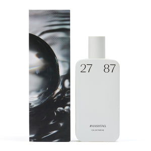 27 87 - #hashtag Parfumflakon in schlichtem Weiß mit klarer Typografie neben künstlerischer Verpackung vor weißem Hintergrund