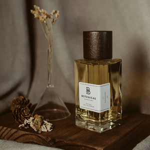 Botanicae - Highlands Parfumflakon mit honigfarbenem Duft und dunklem Holzverschluss auf Holzbrett vor sanftem Stoffhintergrund