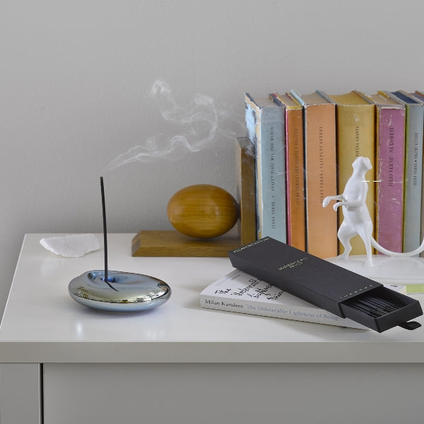 Pigmentarium - Holder - Platinum Wave glänzendes silbernes Design mit brennendem Räucherstäbchen auf weißem Tisch