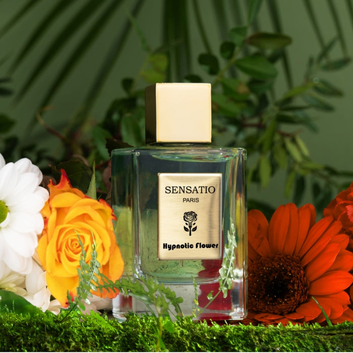 Sensatio Paris - Hypnotic Flower zeigt klaren Flakon mit goldenem Deckel und floralem Etikett vor grünem Pflanzenhintergrund