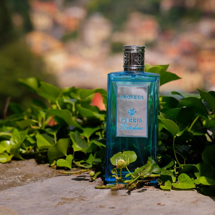 Perris Monte Carlo - Portofino - In Riviera blauer Flakon mit silbernem Verschluss umgeben von grünem Laub vor verschwommener Kulisse